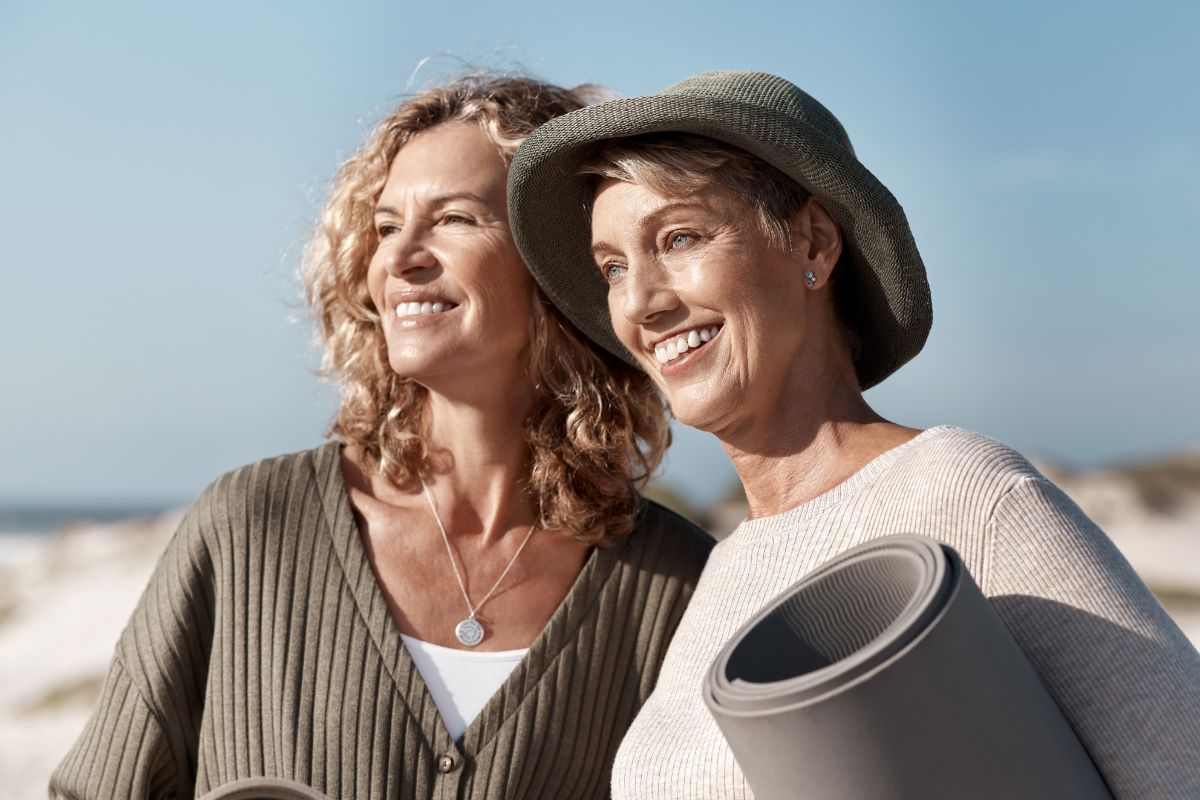 Two smiling women carrying yoga mats on the beach