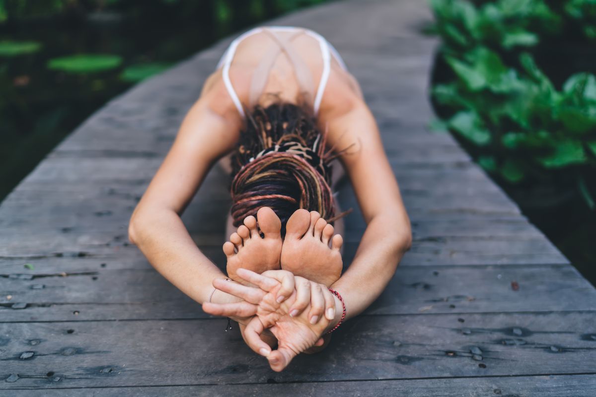 A woman stretching on a wooden path surrounded by greenery